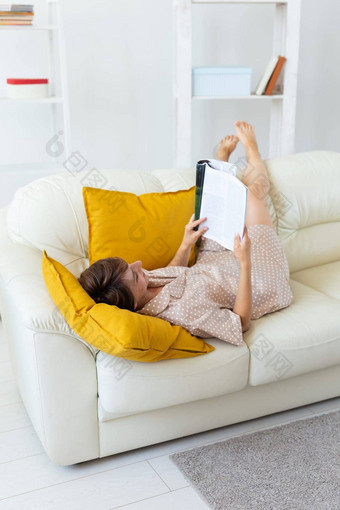 微笑女人说谎杂志舒适的沙发上生活房间睡衣家居服免费的时间假期首页概念