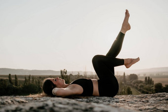 健身女人中间岁的女人长头发健身教练紧身裤上衣伸展运动普拉提岩石森林女健身瑜伽例程概念