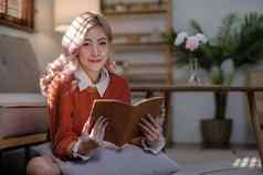 有吸引力的年轻的亚洲女人坐在最小的舒适的生活房间享受阅读书