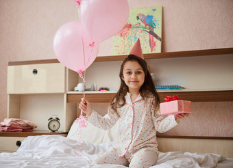 女孩睡衣生日他持有群粉红色的<strong>气球</strong>礼物盒子<strong>坐</strong>着床上微笑相机