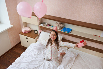 前视图生日女孩聚会，<strong>派</strong>对他持有群粉红色的气球礼物盒子坐着床上<strong>微</strong>笑相机