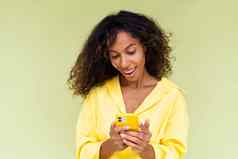 美丽的非洲美国女人休闲衬衫绿色背景持有移动电话微笑