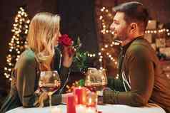 持有美丽的红色的玫瑰年轻的可爱的夫妇浪漫的晚餐在室内