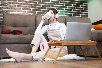 漂亮的年轻的女人移动PC坐在地板上首页一边视图年轻的女自由职业者移动PC电脑杯热喝首页工作首页概念