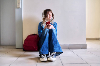 十几岁的学生耳机背包智能手机坐着地板上墙