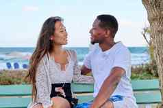 年轻的多元文化的夫妇微笑会说话的坐着板凳上海背景