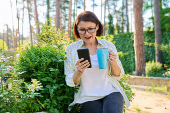 中年女人休息春天花园杯茶智能手机手