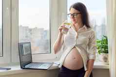 年轻的怀孕了女人喝柠檬水站窗口