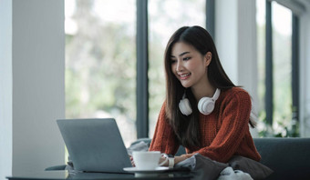 亚洲年轻的女人听音乐耳机流媒体音乐移动PC沙发放松首页