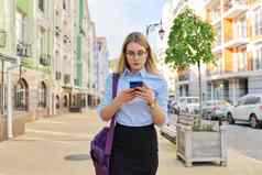 年轻的业务女人智能手机走城市街