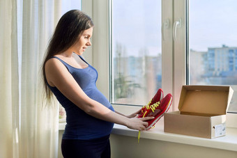 年轻的怀孕了女人持有盒子运动鞋