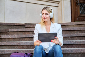 年轻的女人耳机数字平板电脑放松坐着步骤城市