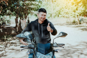 骑摩托车的人摩托车持有安全头盔拇指概念微笑摩托车骑自行车的人持有安全头盔骑摩托车的人男人。给拇指持有安全头盔