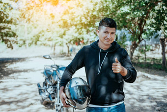 肖像骑摩托车的人持有安全头盔拇指微笑骑摩托车的人男人。持有安全头盔路骑摩托车的人给拇指持有安全头盔路