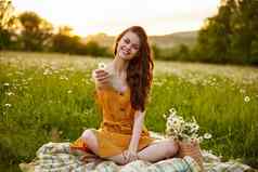 快乐红色头发的人女人坐着洋甘菊场格子莲花位置持有花手微笑相机