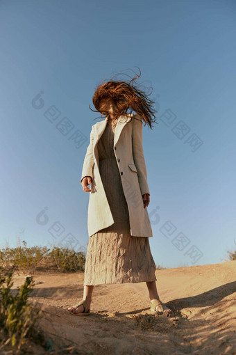 女人时尚夹克长裙子提出了站沙子背景清晰的天空覆盖脸头发运动