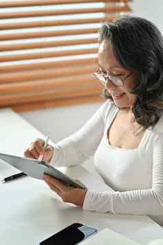 微笑成熟的女人阅读新闻在线检查社会媒体数字平板电脑首页上了年纪的技术概念