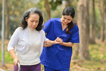 女医疗工人帮助高级女人走康复公园援助康复概念