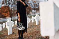 花手年轻的女人黑色的衣服参观墓地白色十字架概念葬礼死亡