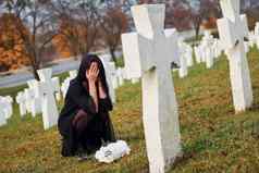 花手年轻的女人黑色的衣服参观墓地白色十字架概念葬礼死亡