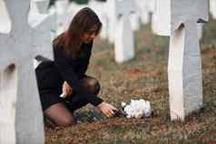 尊重把花年轻的女人黑色的衣服参观墓地白色十字架概念葬礼死亡