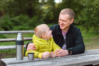 快乐家庭父亲孩子男孩儿子玩笑秋天公园坐着木板凳上表格父亲孩子有趣的在户外玩父亲儿子坐着板凳上会说话的热水瓶