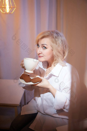 成人成熟的女人年杯咖啡巧克力饼干休闲白色衬衫蓝色的牛仔裤平静舒适的晚上大气透明的窗帘软温暖的灯