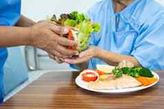 亚洲上了年纪的女人病人吃大马哈鱼牛排早餐蔬菜健康的食物坐着饿了床上医院