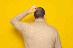 拉美裔男人。穿米色高领毛衣抓头回来相机概念怀疑担心孤立的黄色的背景