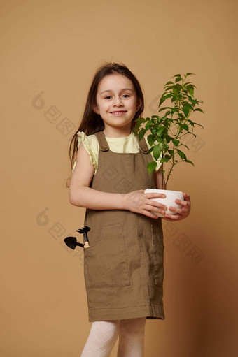 高加索人女孩携带开花胡椒植物花园工具米色背景梦想园丁