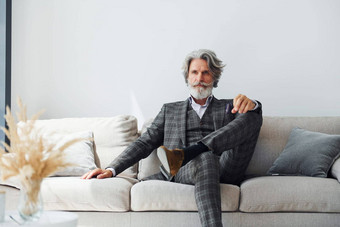 坐在舒适的沙发正式的衣服高级时尚的现代男人。灰色头发胡子在室内
