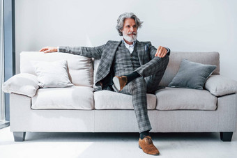 坐在舒适的沙发正式的衣服高级时尚的现代男人。灰色头发胡子在室内