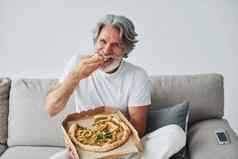吃美味的披萨看显示高级时尚的现代男人。灰色头发胡子在室内