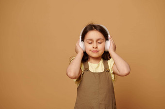 快乐女孩听配乐耳机享受舒缓的音乐眼睛关闭米色背景图片