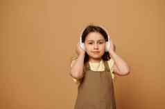 可爱的高加索人孩子女孩听舒缓的音乐无线耳机微笑相机米色背景