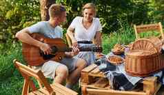 美丽的积极的夫妇野餐在户外男人。玩声吉他女朋友