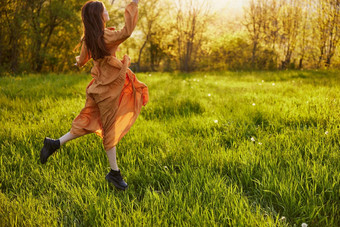 快乐女人橙色衣服照亮射线设置太阳幸福的跳跃绿色场公园享受自然温暖的夏天一天水平照片