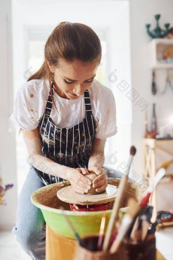 年轻的女陶艺家工作陶器轮在室内使手工制作的粘土产品