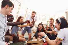 干杯瓶啤酒集团年轻的人休闲衣服聚会，派对屋顶白天
