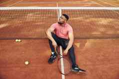 坐在网采取打破非洲美国男人。粉红色的衬衫坐在网球球拍法院在户外