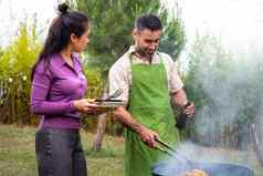 亚洲年轻的女人帮助高加索人男人。烹饪食物烧烤烧烤在户外复制空间