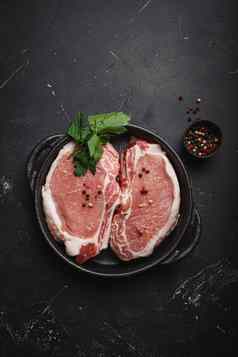减少生肉猪肉牛排调味料黑色的投铁锅黑暗乡村石头背景前视图准备好了烤猪肉腰部排烹饪