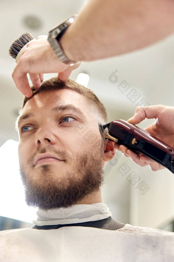 理发师修<strong>剪头发</strong>限幅器英俊的有胡子的男人。