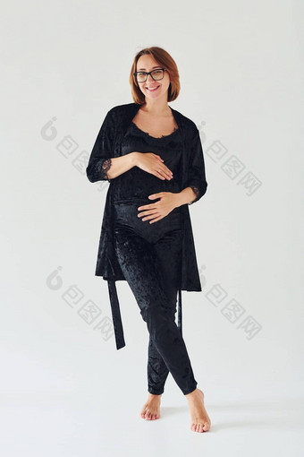 怀孕了年轻的女人睡衣眼镜站在室内白天白色背景