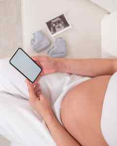 不知名的怀孕了女人坐在白色沙发持有智能手机胎儿超声波筛选