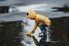 孩子黄色的防水斗篷靴子玩纸手工制作的船玩具在户外雨