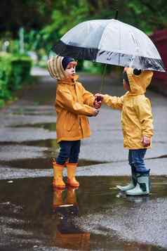 孩子们伞黄色的防水斗篷靴子玩在户外雨