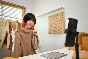 美丽的亚洲女人显示衣服前面智能手机相机销售衣服在线流媒体