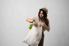 微笑女人t恤他持有可重用的棉花购物袋蔬菜面包绿色概念塑料浪费塑料免费的可持续发展的生活方式