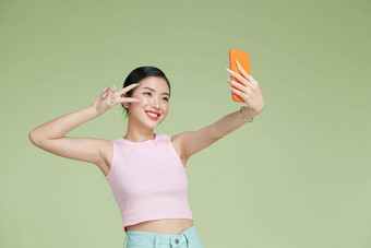 图像很高兴亚洲女人笑显示和平标志采取自拍照片手机